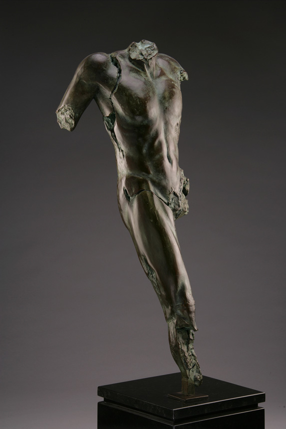Entitled Maped F1, this is a photo of a fragment of a one-quarter life size bronze sculpture. Depicted is a standing nude male figure missing his left leg at the hip and right leg below the knee, both arms and head. By sculptor Blake Ward