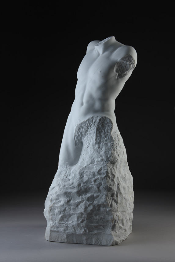 Entitled Layton, this is a photograph depicting a one-quarter life-size marble sculpture of a standing male figure emerging from the stone base, created by sculptor Blake Ward